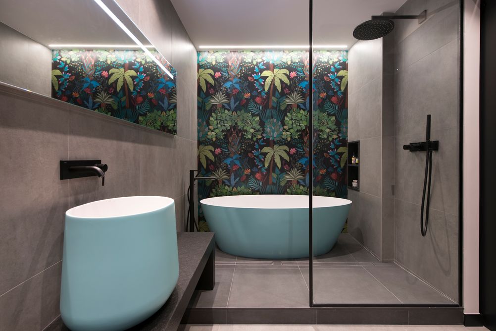 Baño tipo suite con ducha y bañera exenta. Baldosas de gran formato en gris y mural colorido