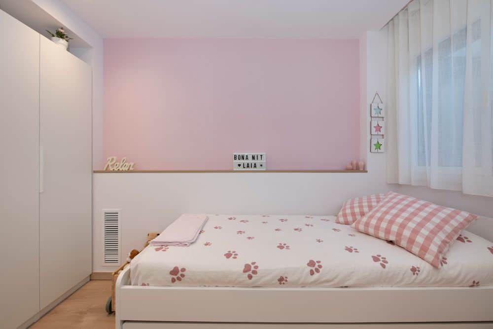 Murete con repisa al lado de la cama. Pintado en blanco en la zona baja y papel pintado en rosa en la parte superior. Habitación juvenil