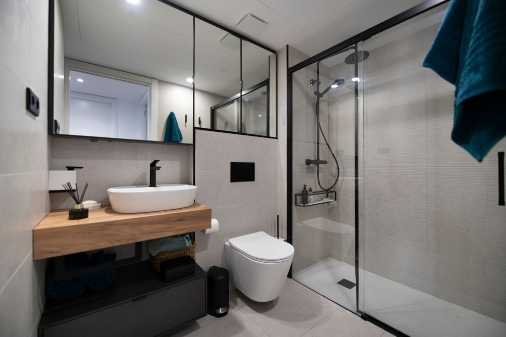 Bany amb perfil mampara i moble mirall negre. Pisca sobre prestatge de fusta