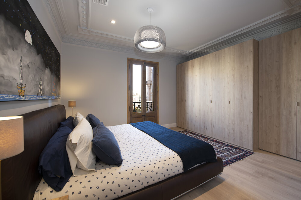 Dormitorio principal con molduras en los techos. Armario y parquet en acabado madera clara. Balconeras de madera.