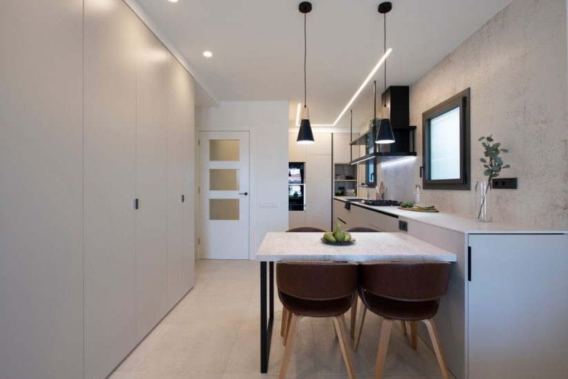 Mesa de comedor unida al mueble de cocina. Con dos lámparas colgantes