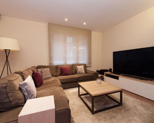 Espacio de sofá esquinero con mesita y televisión TV. Reforma de pisos en Barcelona.