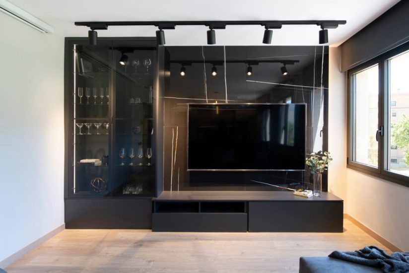 Moble TV negre amb vitrina que s'il·lumina. Paret revestida de ceràmica de gran format en brillant i vetes daurades.