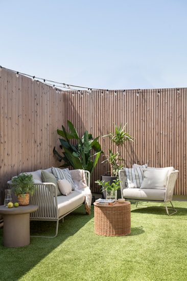 Zona chill out con sofá y butacas de exterior. Con césped artificial y guirnaldas para la iluminación. Reforma de terraza de un ático.