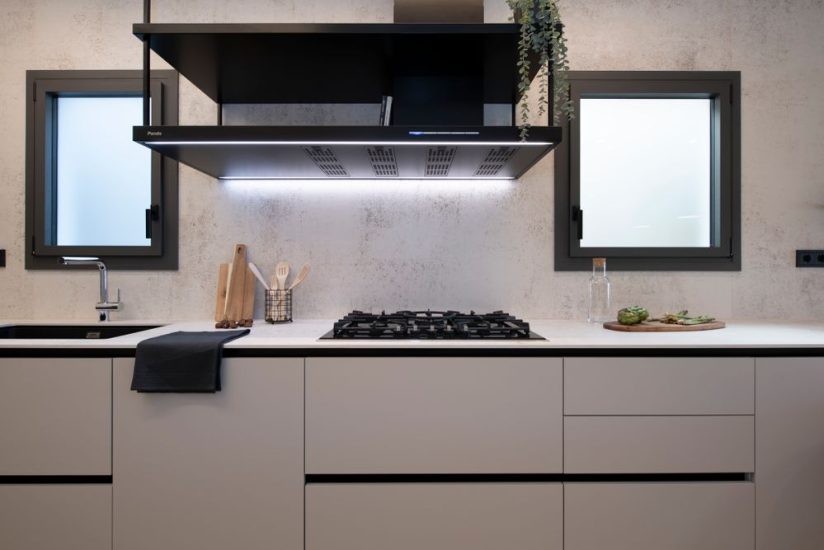 Zona de fogones de gas con gran campana decorativa negra con dos estantes. Del fabricante Pando.