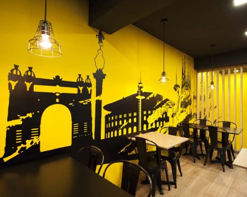 Paret amb vinil skyline barcelona en color groc i negre en una de les parets de la zona de taules. restaurant kyoku