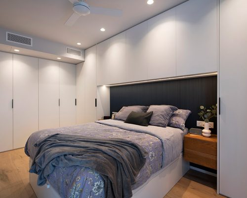 Dormitorio amueblado para conseguir el máximo espacio de almacenaje. Mueble en arco en cabecero de cama. Piso de obra nueva en Barcelona.