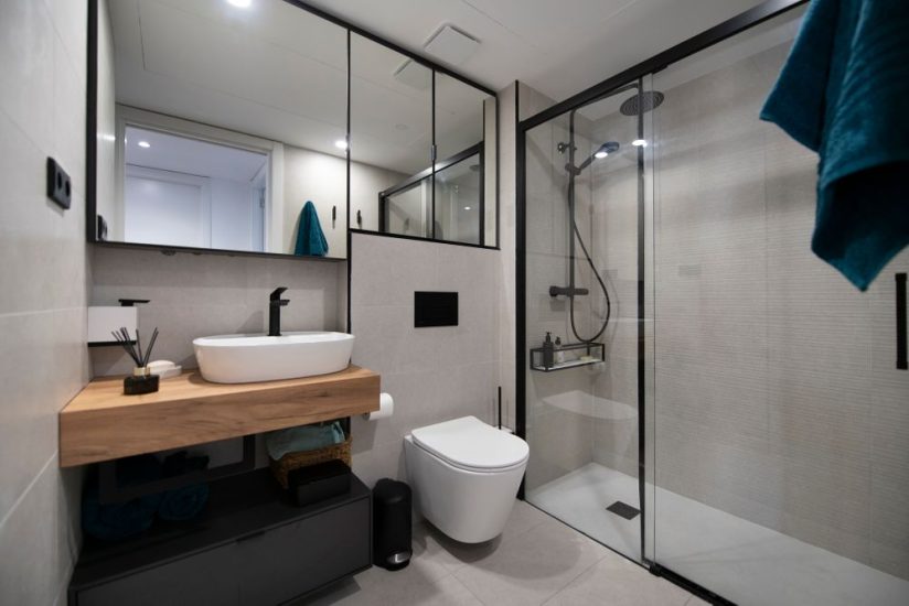 Baño con perfil mampara y mueble espejo en negro. Pisca sobre estante de madera