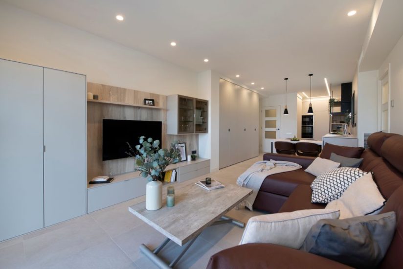 Espacio diáfano con salón, comedor y cocina. Con colores neutros y claros. Sofá color rojo burdeos oscuro