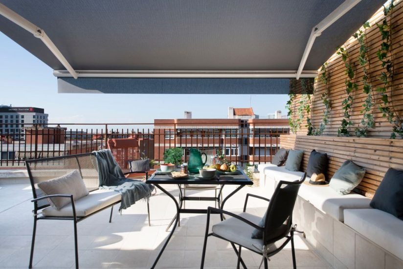 Reforma de terraza con banco de listones de madera y jardín vertical. Toldo oscuro