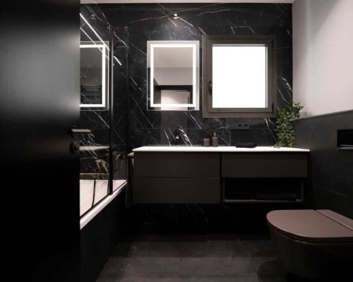 Baño negro sofisticado y elegante. Con revestimiento mármol negro vetas blancas. Mueble y inodoros negros y espejo con luz.