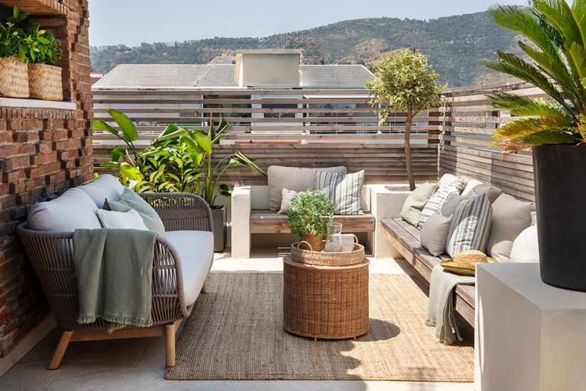 Zona de chill out en una terraza reformada en Barecelona. Compuesta por bancos integrados a las macetas, sofá para exterior, mesita de mimbre y alfombra de Yute.