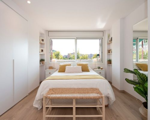 Dormitorio doble en tonos blanco y madera, y con la ventana en el cabecero.