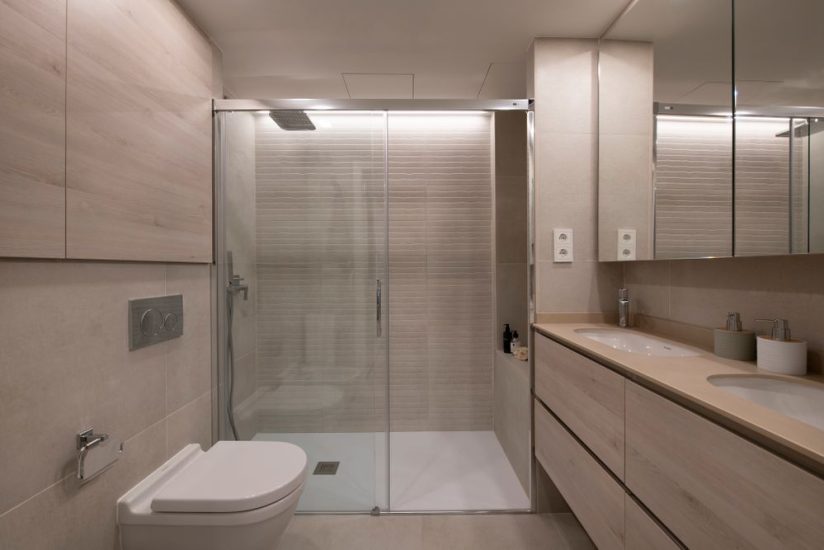 Baño con ducha con tonalidades neutras. Lámpara led y baldosa con textura en la ducha.