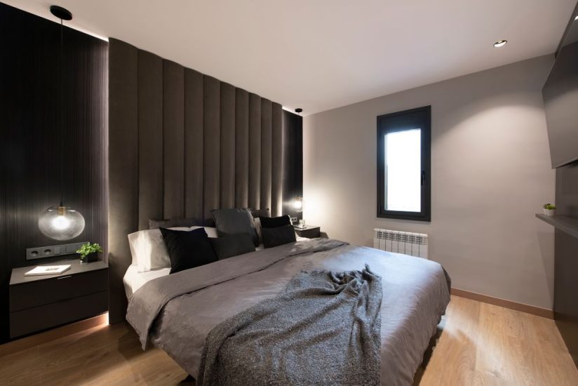 Capçal amb vellut, mural vinílic, llums penjants i tauletes en tonalitats negres i grises