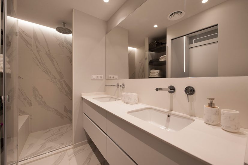 Lavabo con dos picas en color blanco. Revestimientos marmol imitación.