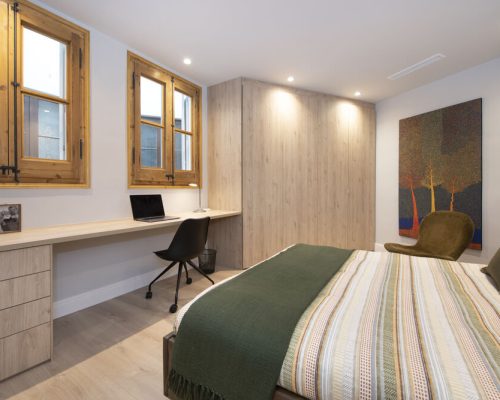 Dormitorio doble con escritorio y armarios de madera tonalidades claras. Con ventanas de madera restauradas.